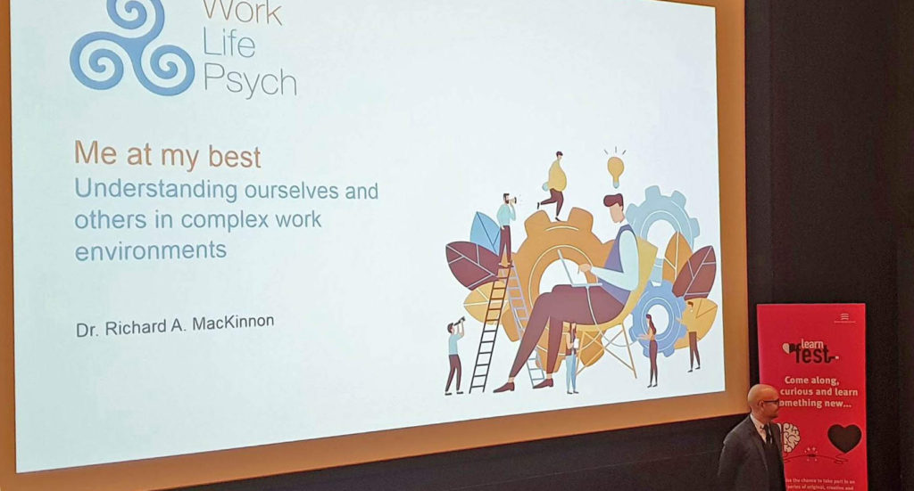 Presentation slide above a man on stage at Learn Fest