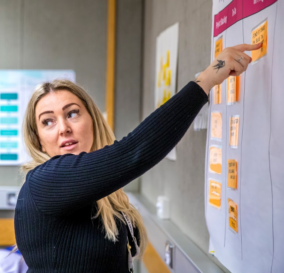 Female pointing to a sticky note on a wall