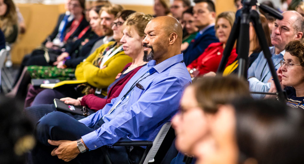 Crowd shot of a number of people in the audience listening to a talk